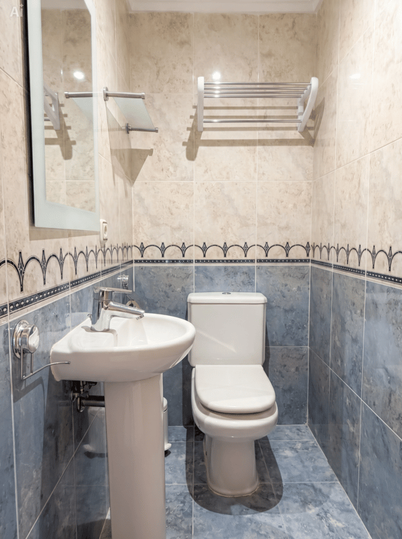 Toilettes d'invités compactes avec lavabo sur pied, WC et murs carrelés bicolores bleu et beige avec frise décorative. Miroir et porte-serviettes inclus.