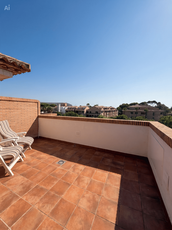 Vaste terrasse extérieure avec carrelage en terre cuite et murs en briques apparentes, aménagée avec deux chaises pliantes rayées. Offre des vues dégagées sur les bâtiments résidentiels et la végétation.