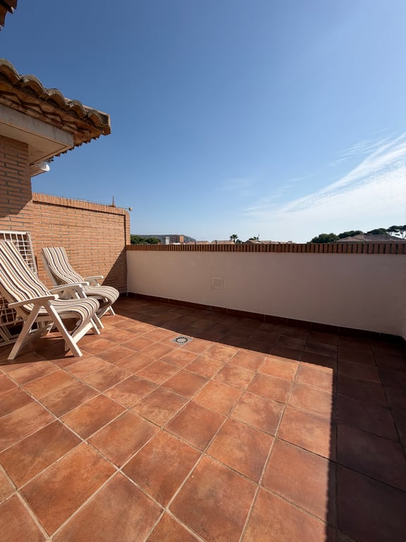 Vaste terrasse supérieure avec carrelage en terre cuite et muret en briques. Deux chaises longues invitent à la détente sous un ciel clair, offrant un espace ensoleillé.