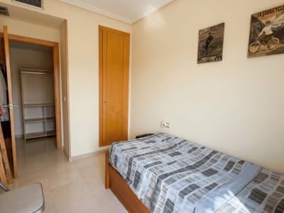 Chambre individuelle avec lit en bois, sol effet marbre clair et armoire intégrée. Un dressing ouvert adjacent et une bouche de climatisation sont visibles.