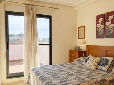 Chambre lumineuse avec un lit double, une tête de lit en bois et un accès direct à une terrasse extérieure. Équipée d'un ventilateur de plafond et d'un sol carrelé clair.