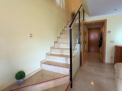 Escalier intérieur en marbre clair avec des bandes antidérapantes rouges et une balustrade moderne en métal noir et verre. Le sol carrelé assorti et la lumière naturelle complètent l'espace.
