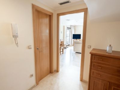 Hall d'entrée lumineux avec sol en marbre clair poli et portes en bois. Un meuble en bois est à droite, ouvrant sur le salon-salle à manger.