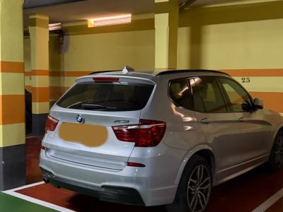 Place de parking souterraine privée avec un SUV argenté, murs jaunes à rayures oranges et tuyaux rouges au plafond. Éclairage fluorescent et sol bicolore.