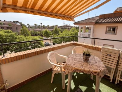 Terrasse extérieure avec gazon synthétique, mobilier de jardin en plastique et store banne rayé. Vues sur la verdure et les résidences.