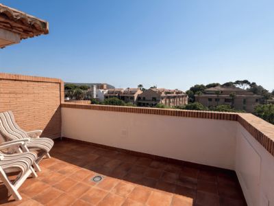 Vaste terrasse extérieure avec carrelage en terre cuite et murs en briques apparentes, aménagée avec deux chaises pliantes rayées. Offre des vues dégagées sur les bâtiments résidentiels et la végétation.