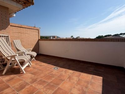 Vaste terrasse supérieure avec carrelage en terre cuite et muret en briques. Deux chaises longues invitent à la détente sous un ciel clair, offrant un espace ensoleillé.