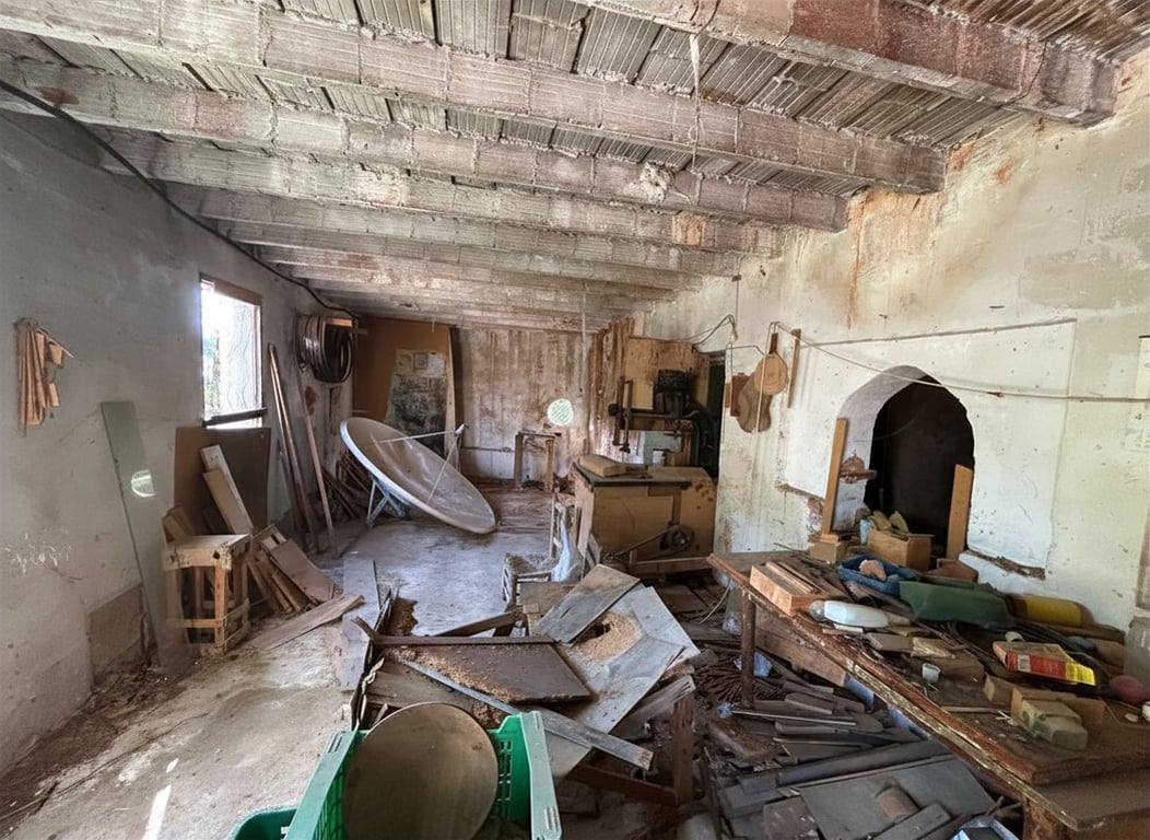Espace intérieur brut avec plafond à poutres en béton apparentes, murs écaillés et alcôve arquée, idéal pour rénovation. La zone contient des débris et du vieil équipement. Espace intérieur brut avec plafond à poutres en béton apparentes, murs écaillés et alcôve arquée, idéal pour rénovation. La zone contient des débris et du vieil équipement.