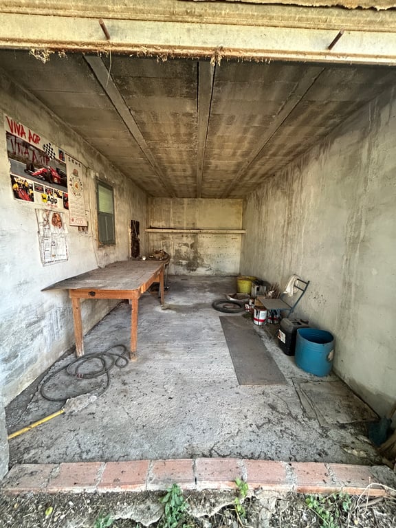 Intérieur d'un garage ou d'un entrepôt avec murs et plafond en béton brut. Une table en bois, une fenêtre et divers objets stockés révèlent un espace nécessitant une rénovation. Intérieur d'un garage ou d'un entrepôt avec murs et plafond en béton brut. Une table en bois, une fenêtre et divers objets stockés révèlent un espace nécessitant une rénovation.