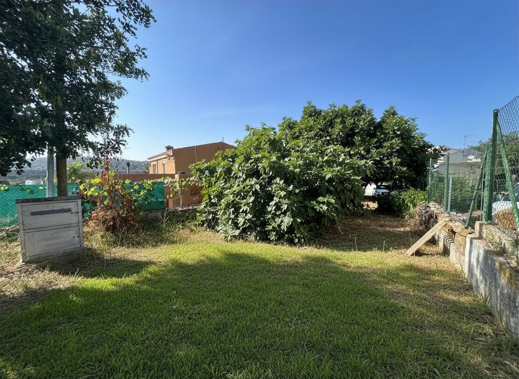 Jardin arrière avec pelouse et végétation mature, dont un grand arbre feuillu. Un mur d'enceinte et un bâtiment traditionnel sont visibles à l'arrière-plan. Jardin arrière avec pelouse et végétation mature, dont un grand arbre feuillu. Un mur d'enceinte et un bâtiment traditionnel sont visibles à l'arrière-plan.