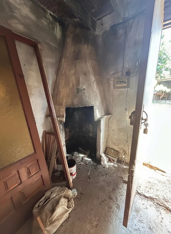 Pièce à rénover avec une cheminée maçonnée traditionnelle, murs bruts et débris au sol. Une porte en bois et une lumière naturelle entrent, révélant un potentiel de transformation. Pièce à rénover avec une cheminée maçonnée traditionnelle, murs bruts et débris au sol. Une porte en bois et une lumière naturelle entrent, révélant un potentiel de transformation.