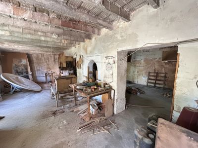 Cet espace intérieur brut révèle des poutres en briques et béton apparentes, des murs non enduits et un sol en béton jonché de débris. Il souligne le besoin d'une rénovation structurelle complète.