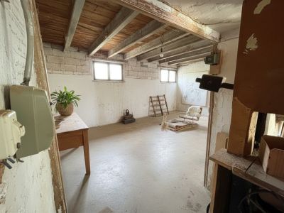 Espace intérieur ouvert avec poutres en bois apparentes au plafond et murs en maçonnerie brute. Deux fenêtres éclairent naturellement cette pièce au sol en béton, prête à être rénovée.