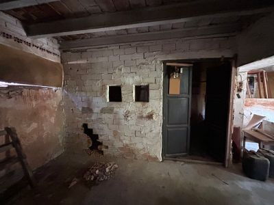 Intérieur brut avec murs en briques apparentes, plafond à poutres en bois et ouvertures. Un espace clair offrant un potentiel de rénovation complète.