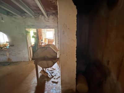 Intérieur en rénovation avec poutres apparentes et murs bruts. Une structure en bois octogonale est visible au centre, avec lumière naturelle au fond.