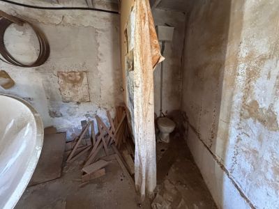 Intérieur en rénovation complète, avec toilettes anciennes, murs écaillés et bois éparpillé, révélant son potentiel de transformation.