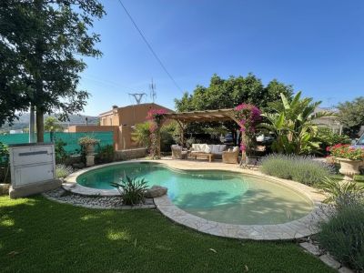 Piscine de forme irrégulière avec margelle en pierre, jouxtant une pergola ornée de bougainvilliers roses, offrant un coin salon ombragé dans un jardin méditerranéen.