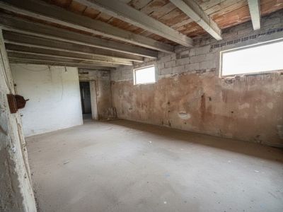 Vaste pièce intérieure avec sol en béton, murs en briques et parpaings apparents, et plafond à poutres en bois et tuiles de terre cuite. Deux petites fenêtres éclairent cet espace à rénover entièrement.