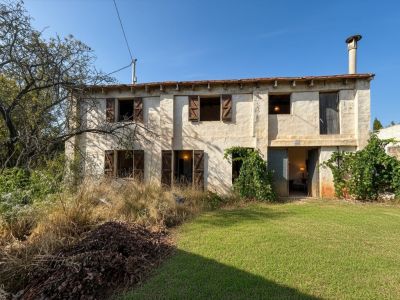 Vue extérieure d'une maison traditionnelle à deux étages avec une façade en stuc patiné, des volets en bois et un vieux toit en tuiles avec cheminée. Le jardin mêle pelouse et végétation sauvage.