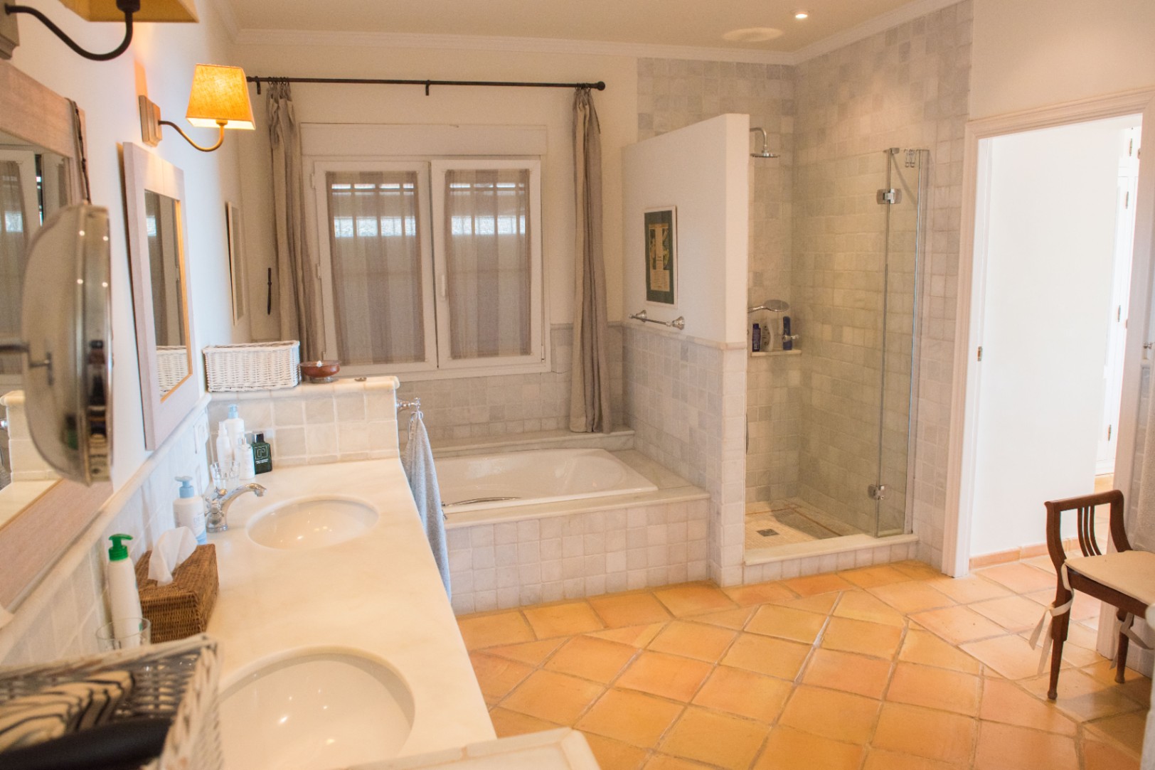 Salle de bain spacieuse avec double vasque en marbre, sol en terre cuite, baignoire encastrée et douche à l'italienne séparée avec paroi vitrée.