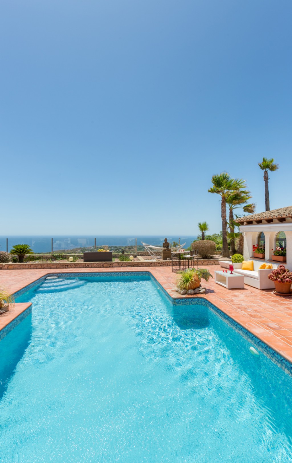 Piscine en mosaïque bleue et terrasse en terre cuite avec coin salon, palmiers et vue panoramique sur la mer Méditerranée à Benitachell.