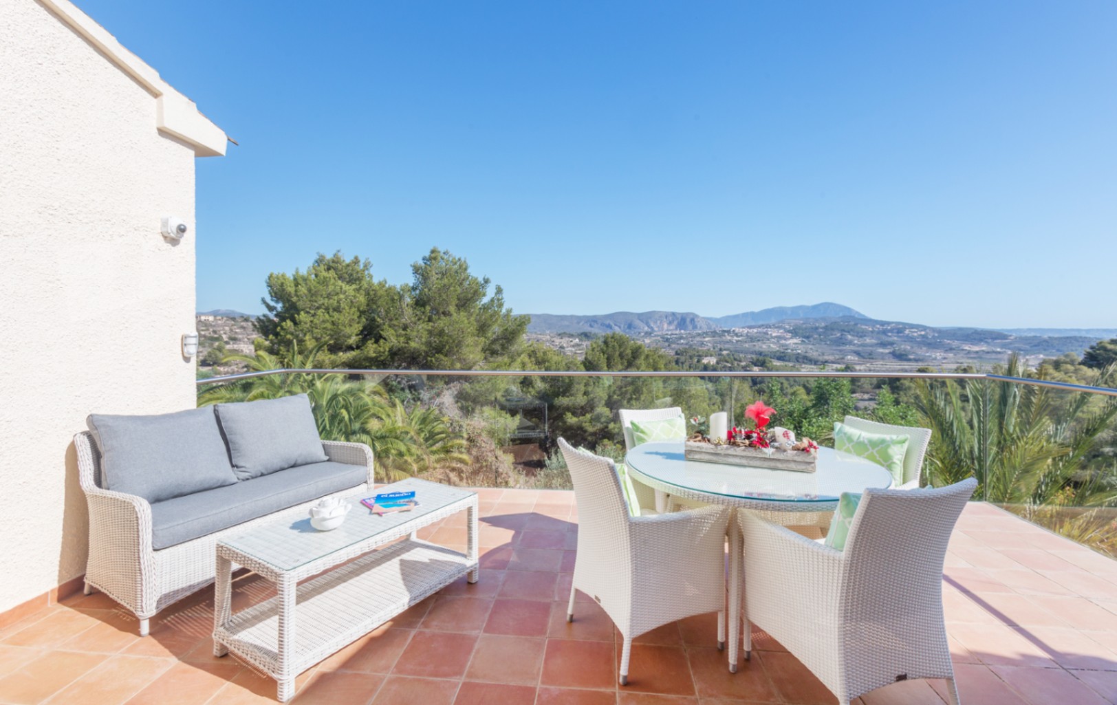 Terrasse carrelée en terre cuite équipée d'un salon de jardin en résine tressée blanche, offrant une vue dégagée sur les montagnes et la végétation méditerranéenne.