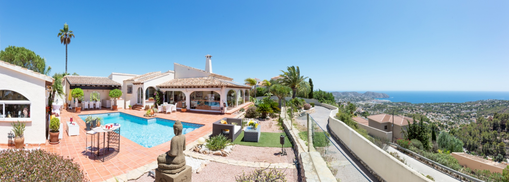 Terrasse panoramique avec carrelage en terre cuite, piscine privée et statue de Bouddha, surplombant la mer Méditerranée et le paysage côtier.