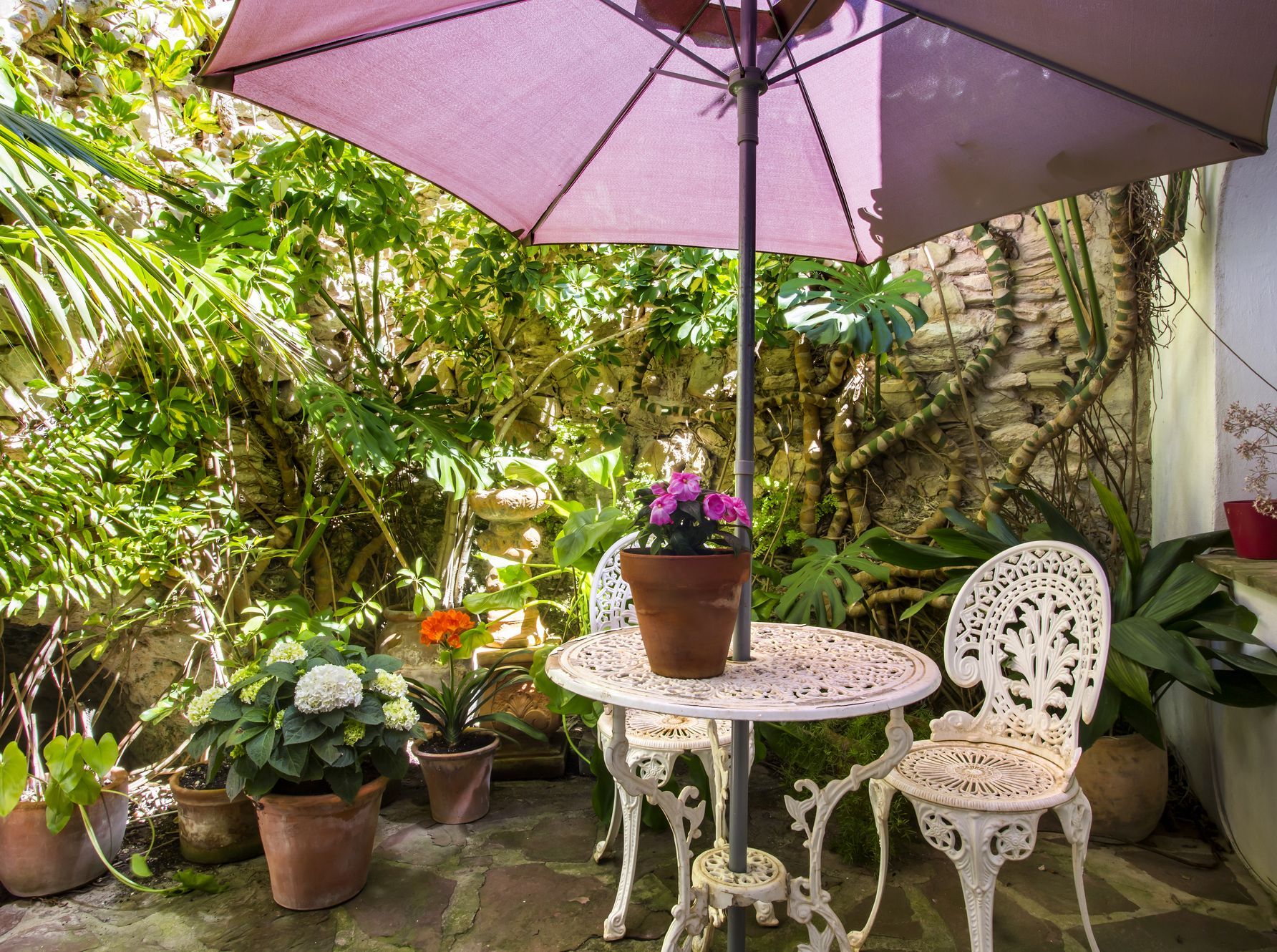 Cour intime avec table en fer forgé, entourée de verdure luxuriante et de murs en pierre.