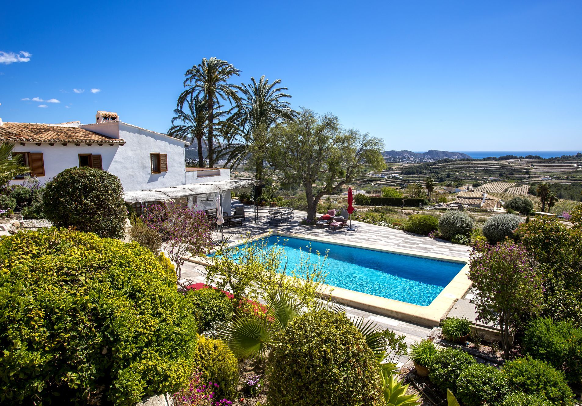 Vue surélevée de la piscine bordée de pierre, entourée de jardins matures et de la maison principale de style méditerranéen.