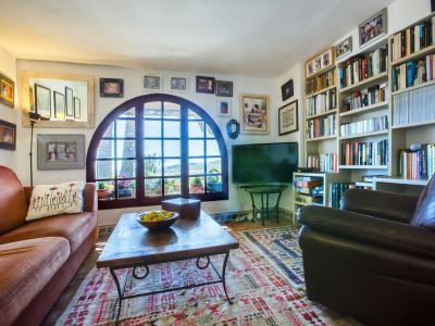 Salon avec fenêtre cintrée et vue, décoré d'un tapis à motifs et d'une bibliothèque remplie de livres.