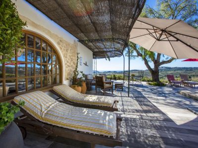Terrasse couverte avec chaises longues en bois et vue sur la mer, abritée par un auvent en roseau.