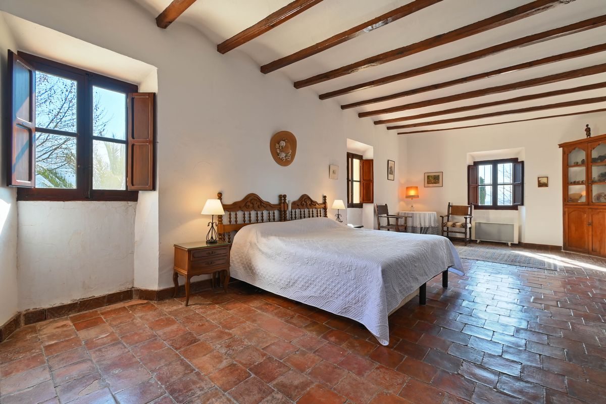 Chambre rustique avec poutres en bois apparentes, sol en terre cuite authentique et mobilier traditionnel en bois sculpté.