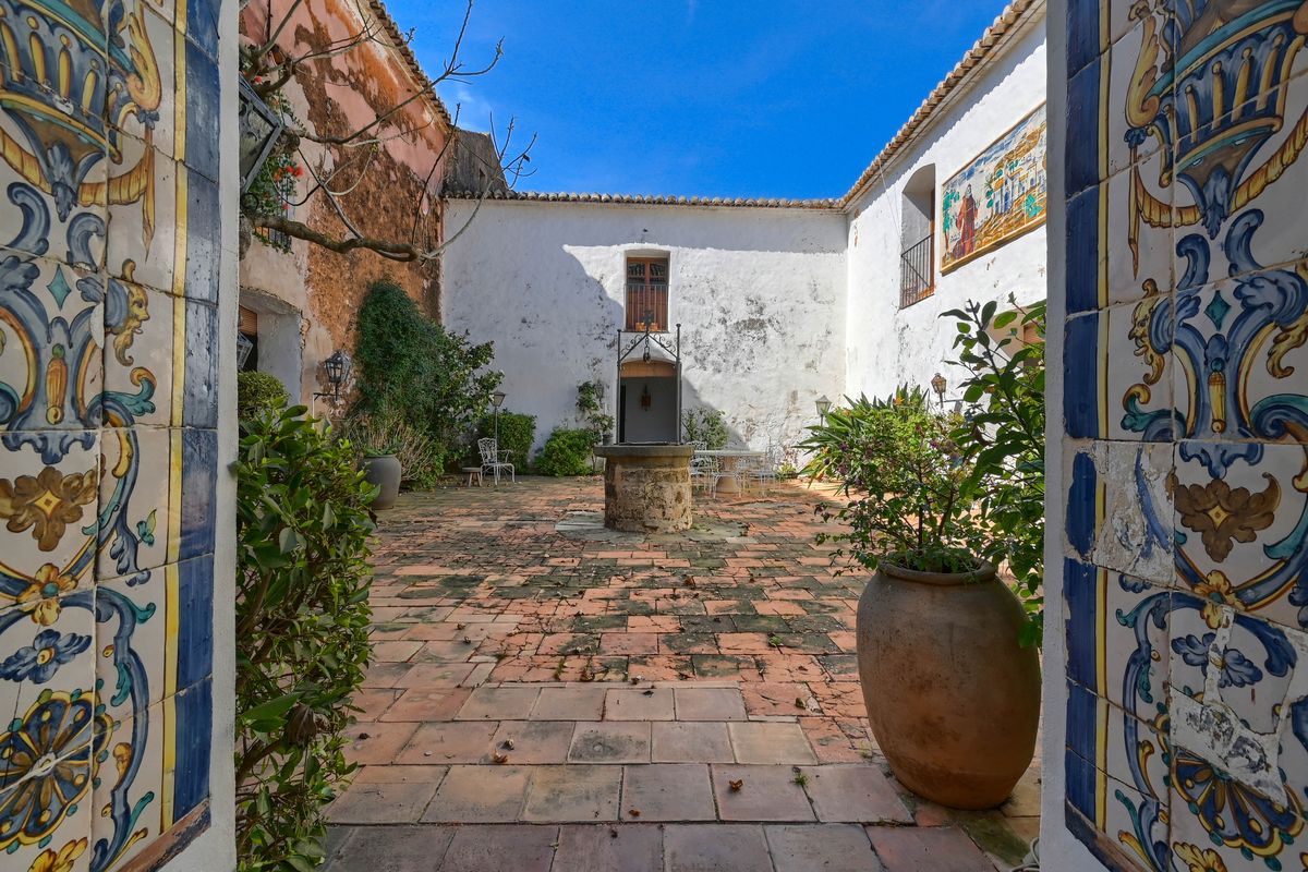 Cour intérieure traditionnelle avec un puits central en pierre, sol en terre cuite et azulejos décoratifs peints à la main sur l'arche d'entrée.