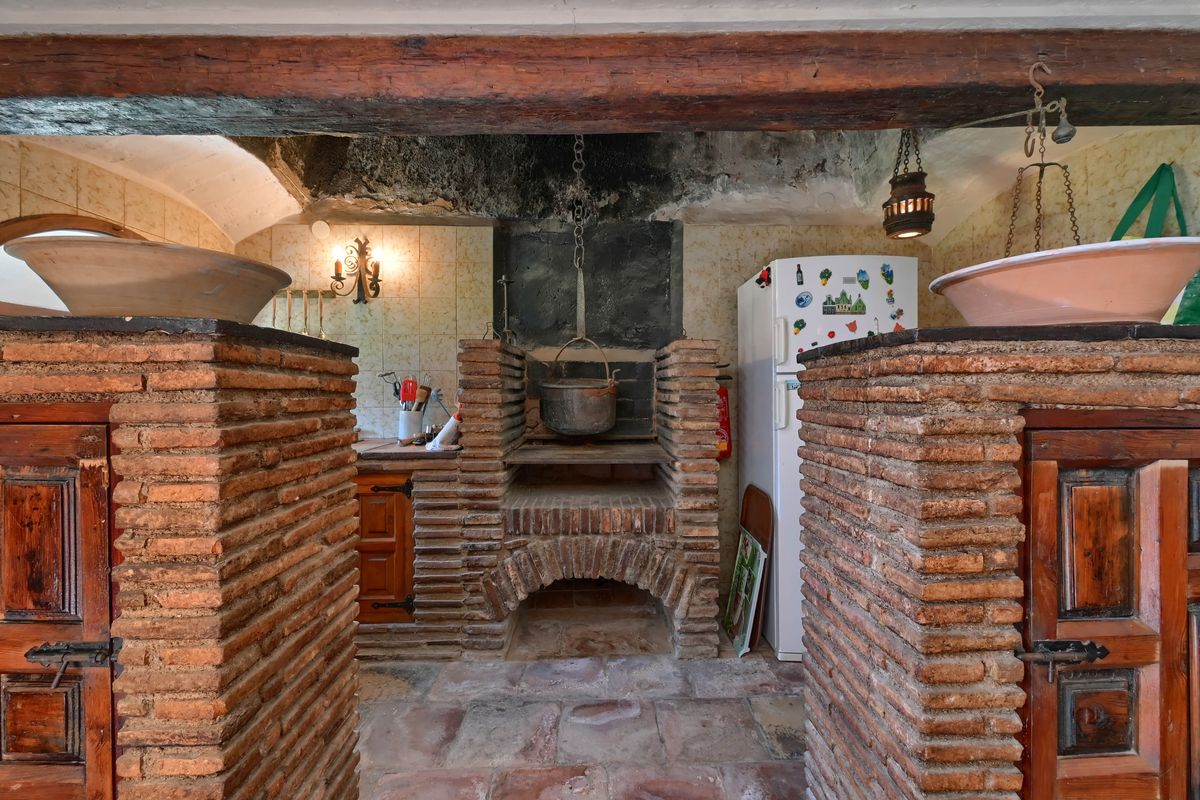 Cuisine historique avec foyer traditionnel en briques, poutres en bois massif et chaudron en fer suspendu au-dessus de l'âtre.