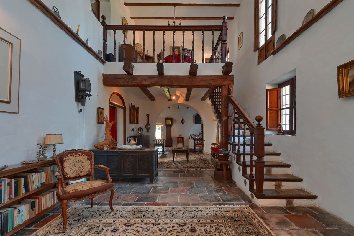 Espace de vie à double hauteur avec poutres apparentes, sol en pierre rustique et une mezzanine surplombant l'intérieur traditionnel.