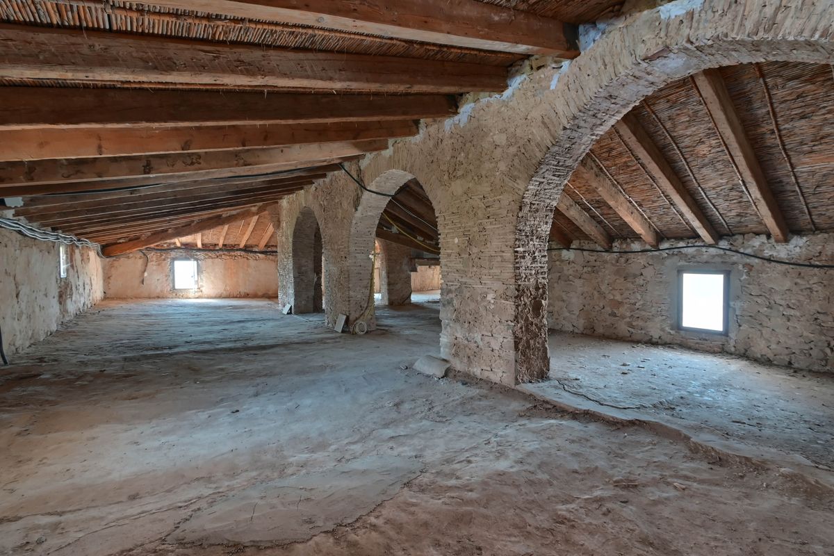 Espace sous combles avec poutres en bois d'origine, plafonds en canisse et arches structurelles en pierre et brique apparente.
