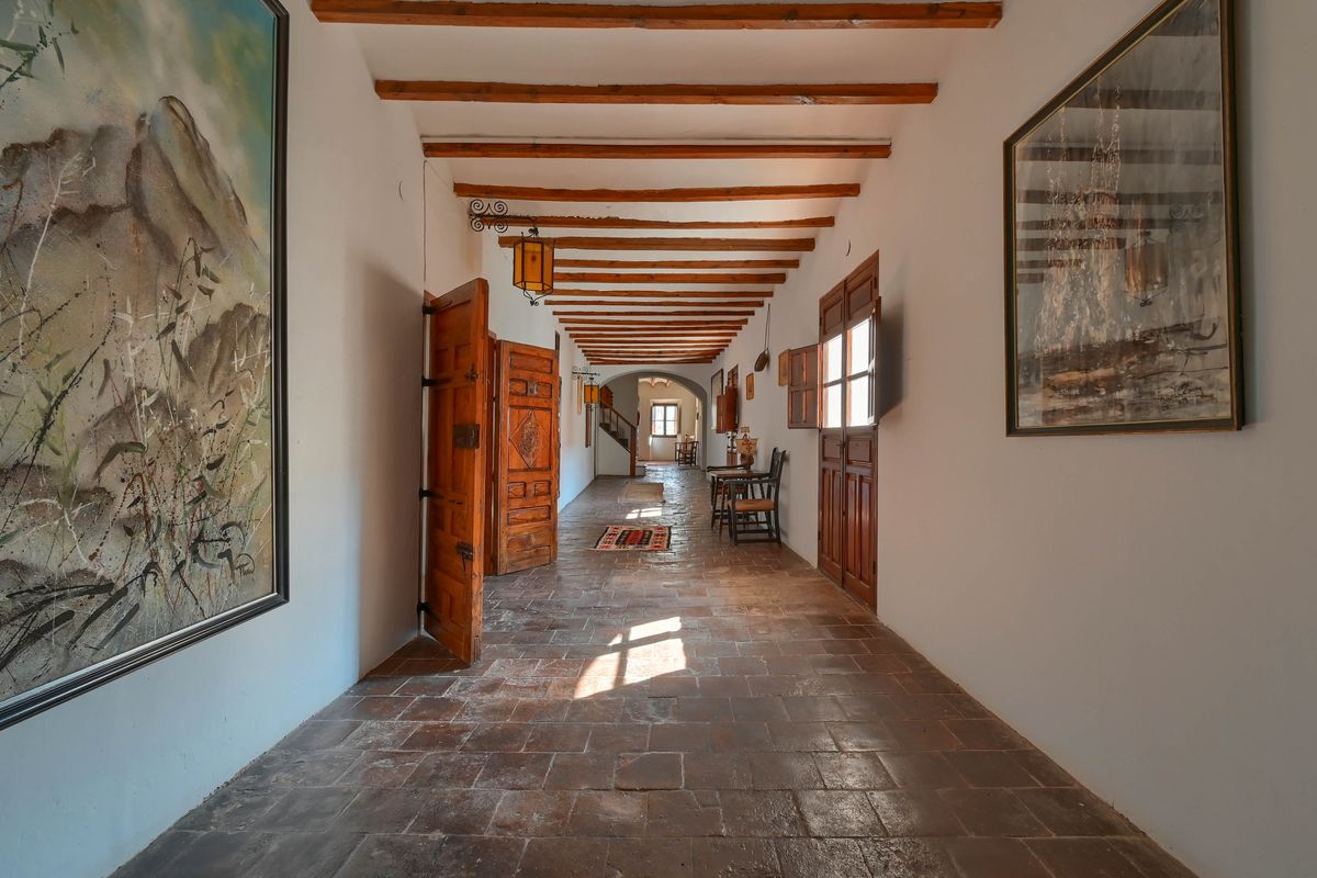 Long couloir avec sol en terre cuite, poutres en bois apparentes et portes massives en bois sculpté illustrant le style rustique de la demeure.