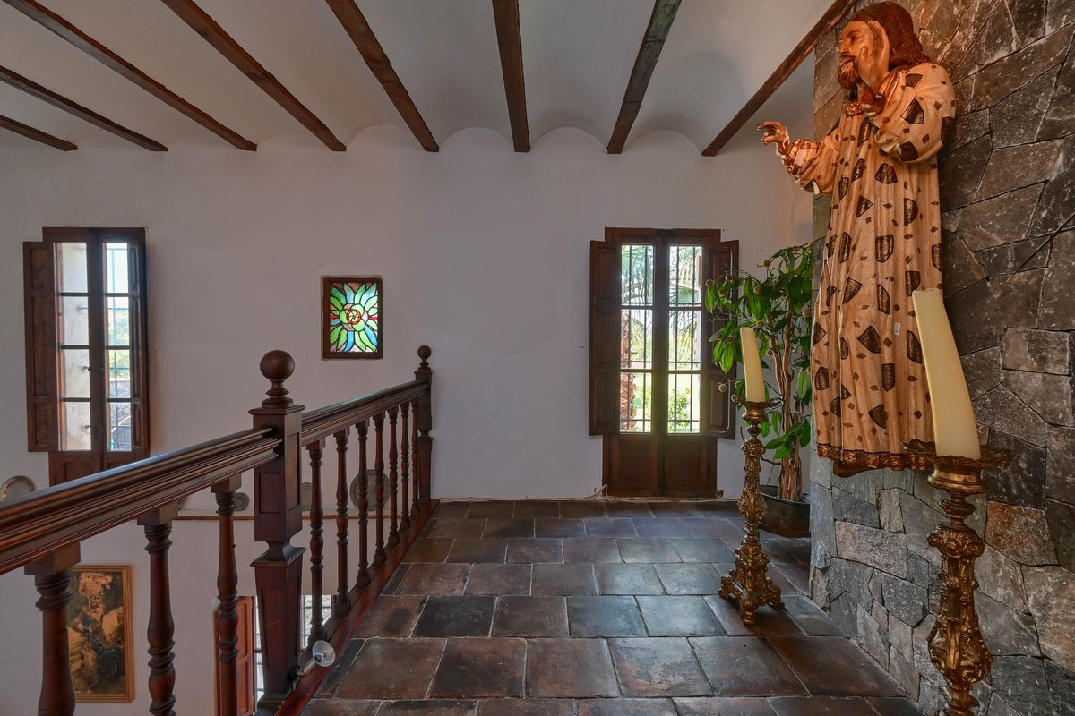 Palier à l'étage avec sol en terre cuite, poutres apparentes, balustrade en bois sculpté et mur en pierre naturelle orné d'éléments décoratifs classiques.