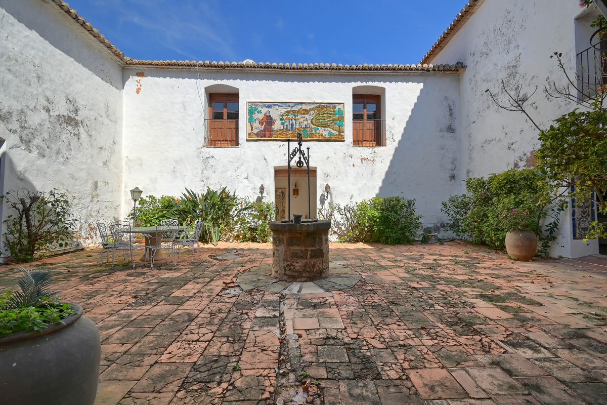 Patio intérieur traditionnel avec sol en terre cuite, puits central en pierre et une grande fresque murale en céramique sur les murs blanchis.