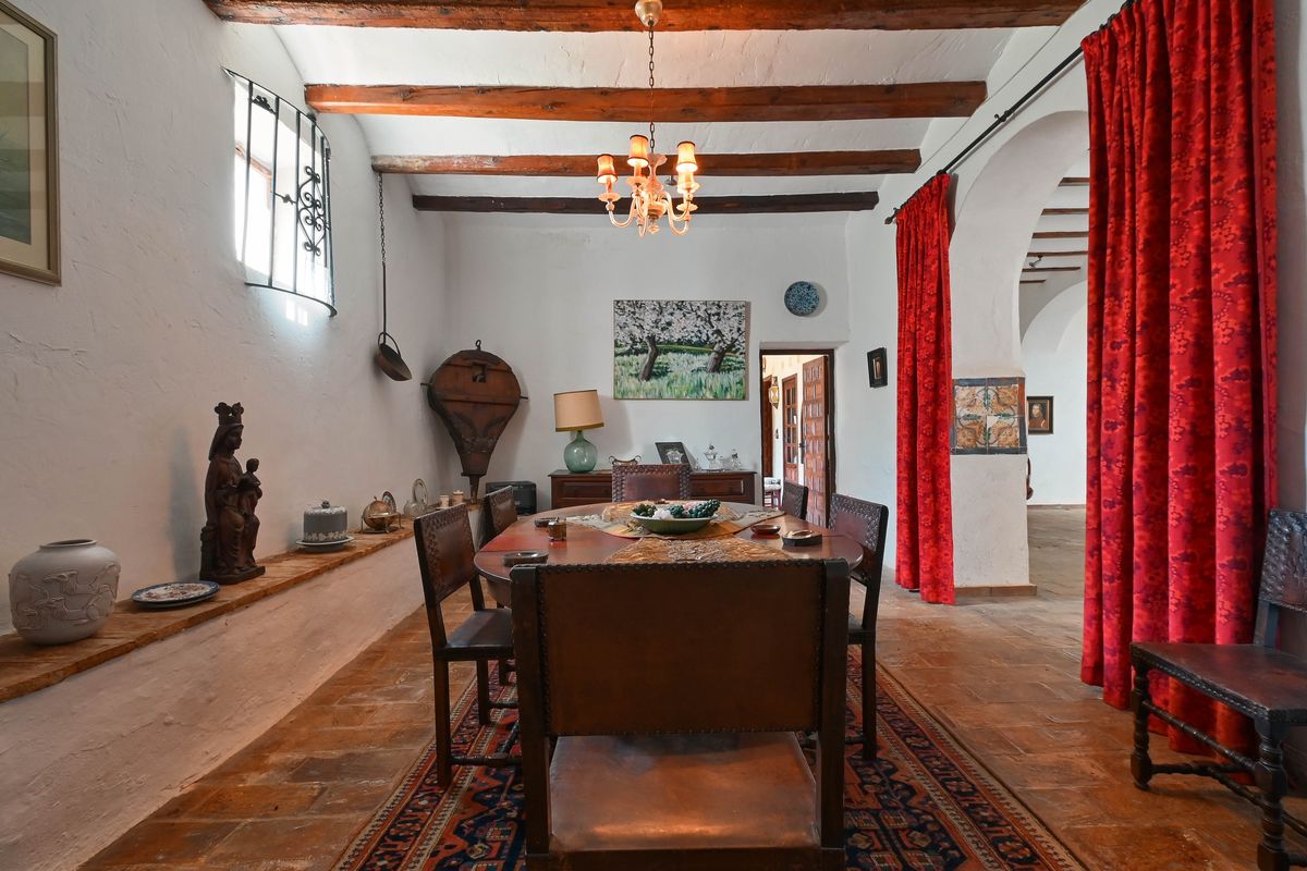 Salle à manger rustique avec poutres en bois apparentes, sol en terre cuite et mobilier traditionnel en cuir près d'une arche voûtée.