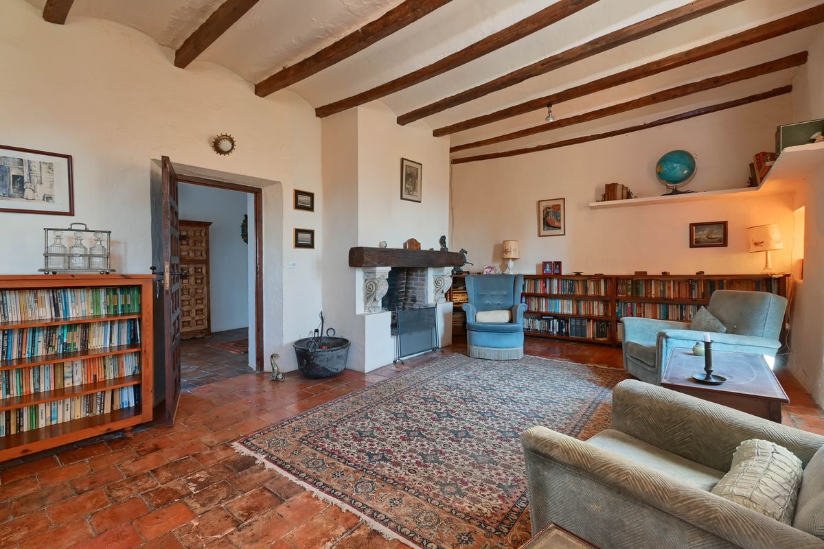 Salon doté de poutres apparentes, d'une cheminée traditionnelle avec linteau en bois, d'un sol en terre cuite et de bibliothèques intégrées.