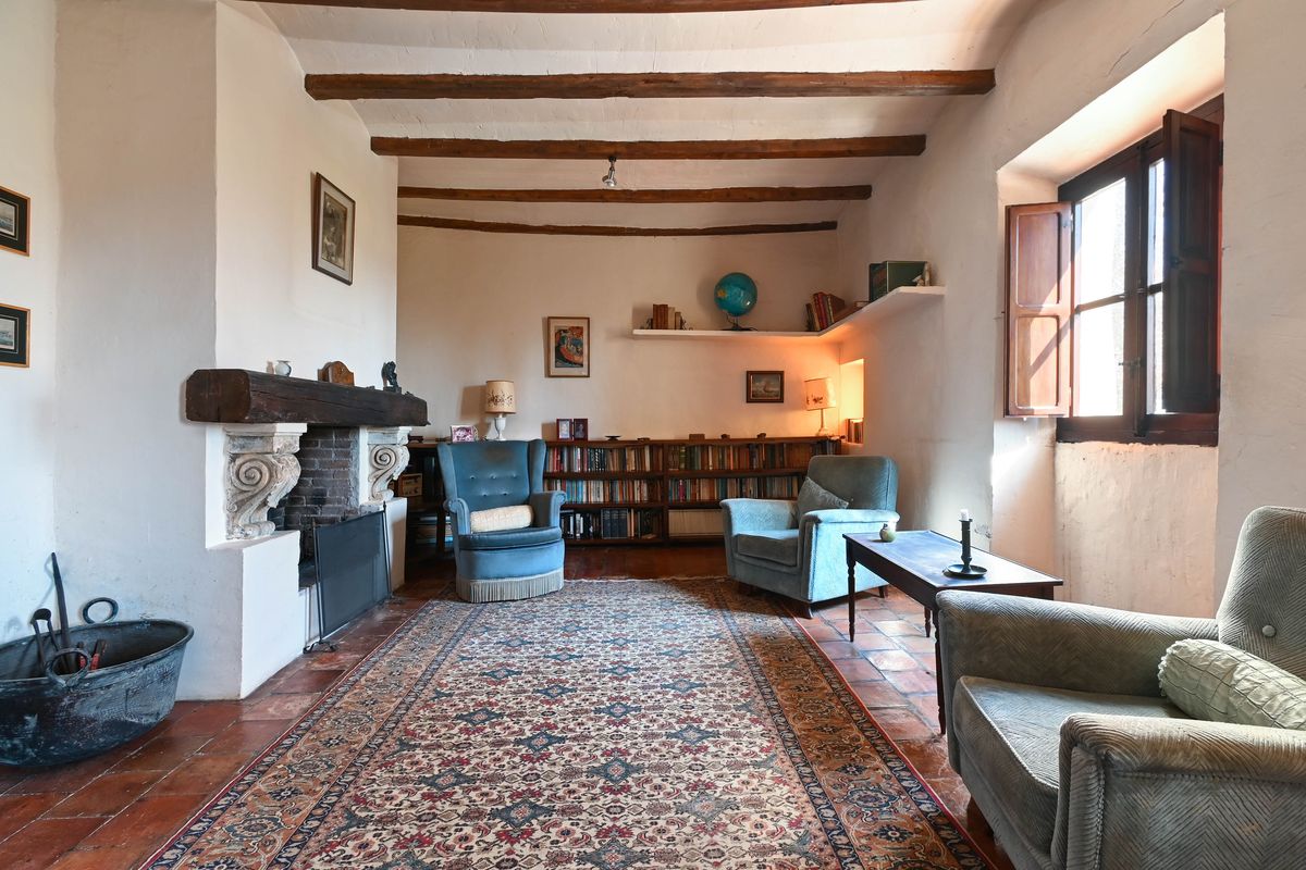 Salon historique avec poutres en bois apparentes, cheminée à linteau massif, sol en terre cuite et bibliothèque intégrée.