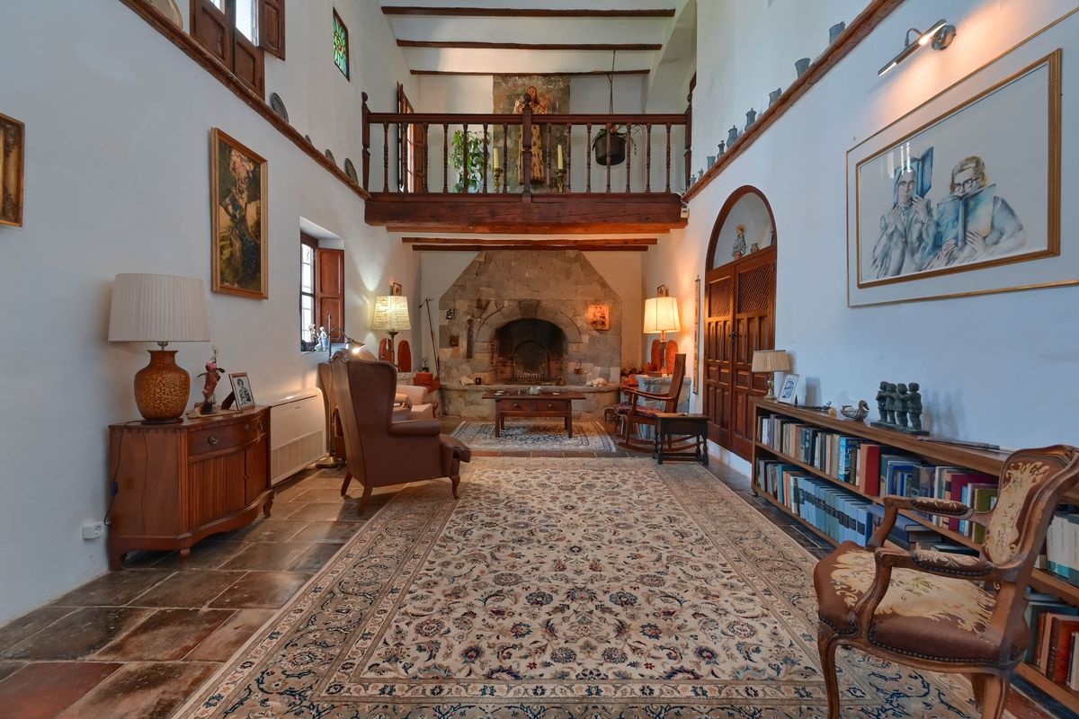 Salon spacieux avec cheminée en pierre, poutres en bois apparentes et mezzanine en bois surplombant l'espace de vie aux sols en terre cuite.