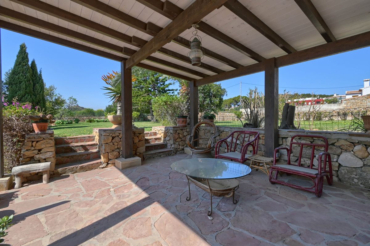 Terrasse couverte avec poutres apparentes en bois, sol en dalles de pierre naturelle et murets en pierre sèche ouvrant sur le jardin.