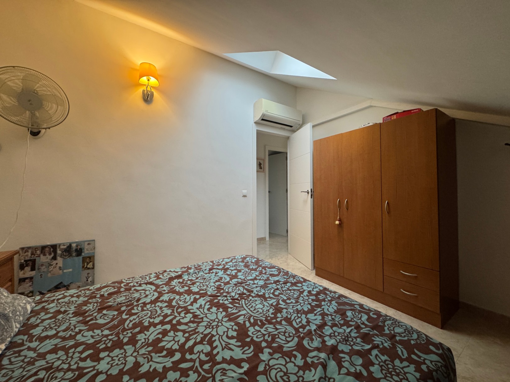 Chambre avec couvre-lit à motifs, armoire en bois et éclairage d'ambiance chaleureux.