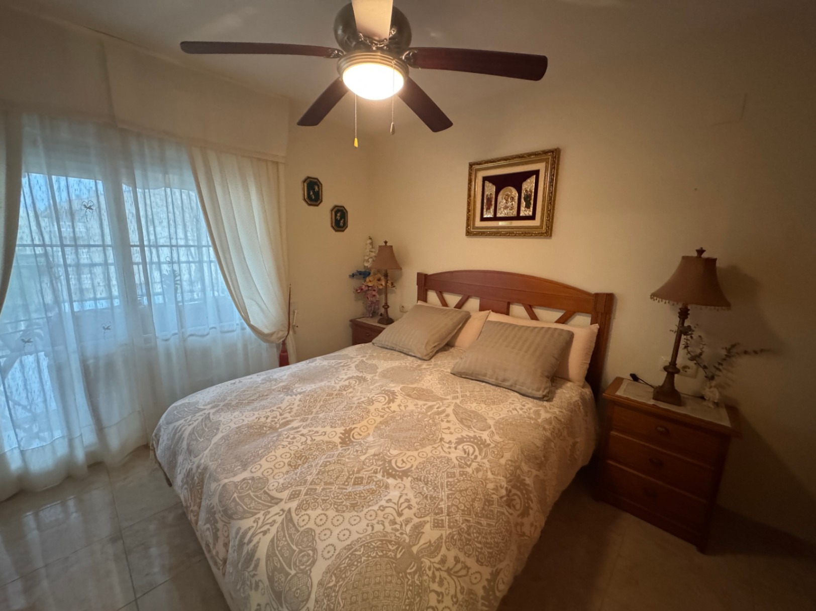 Chambre avec lit en bois, literie à motifs et ventilateur de plafond avec lumière intégrée.