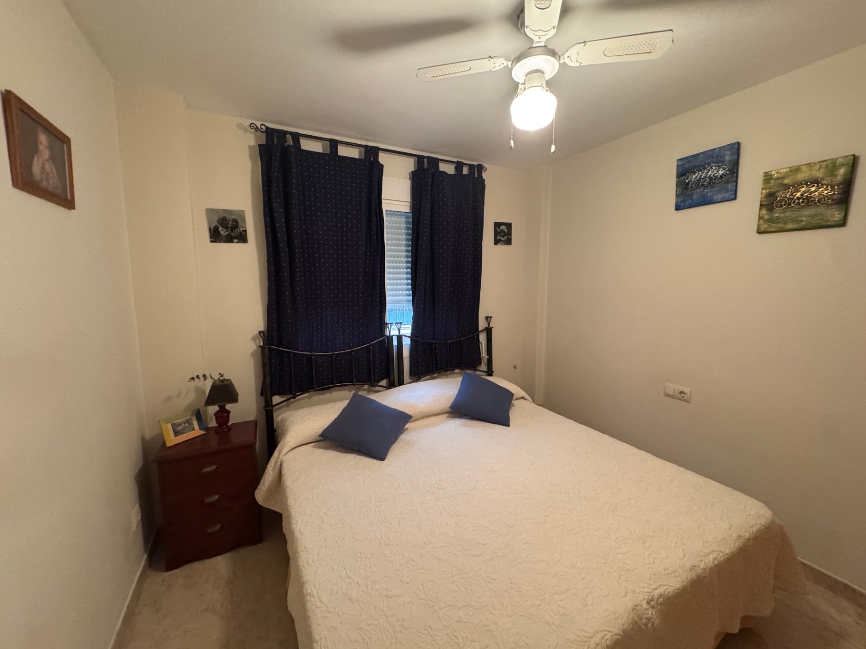 Chambre lumineuse avec lit double, rideaux bleu marine et table de chevet en bois.