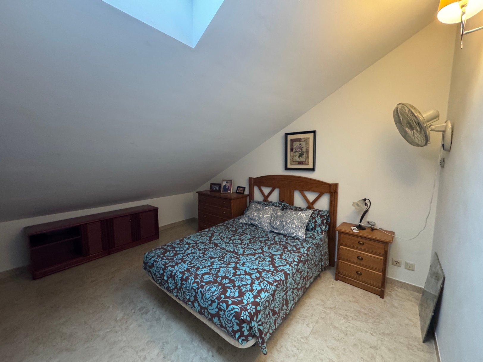 Chambre mansardée avec lit double, commode en bois et lucarne.