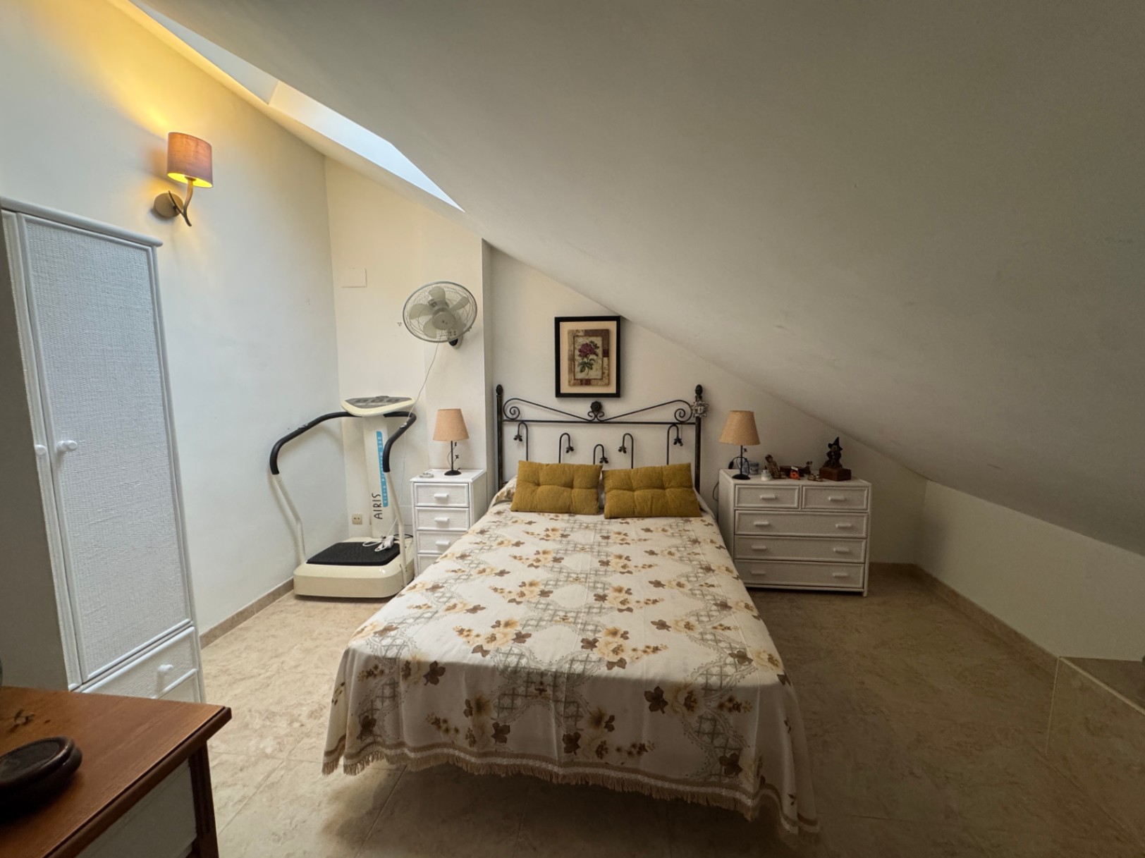 Chambre mansardée avec lit double, machine d'exercice et armoires blanches.