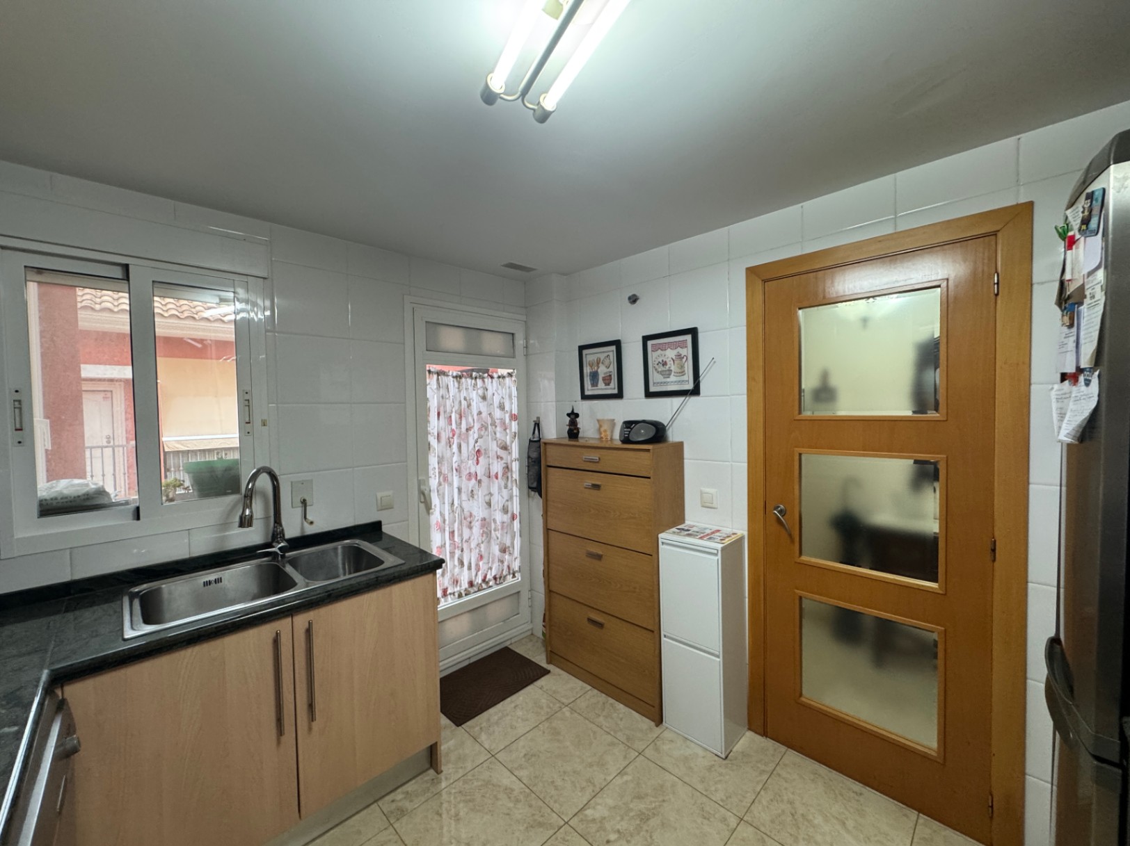 Cuisine fonctionnelle avec comptoir en granit noir, carrelage en céramique et porte en bois avec panneaux de verre.